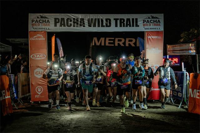 Pelotón saliendo del arco de partida en plena madrugada, iluminado solo por linternas frontales