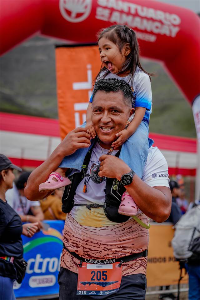 Corredor cargando a su hija en hombros bajo el arco del Santuario