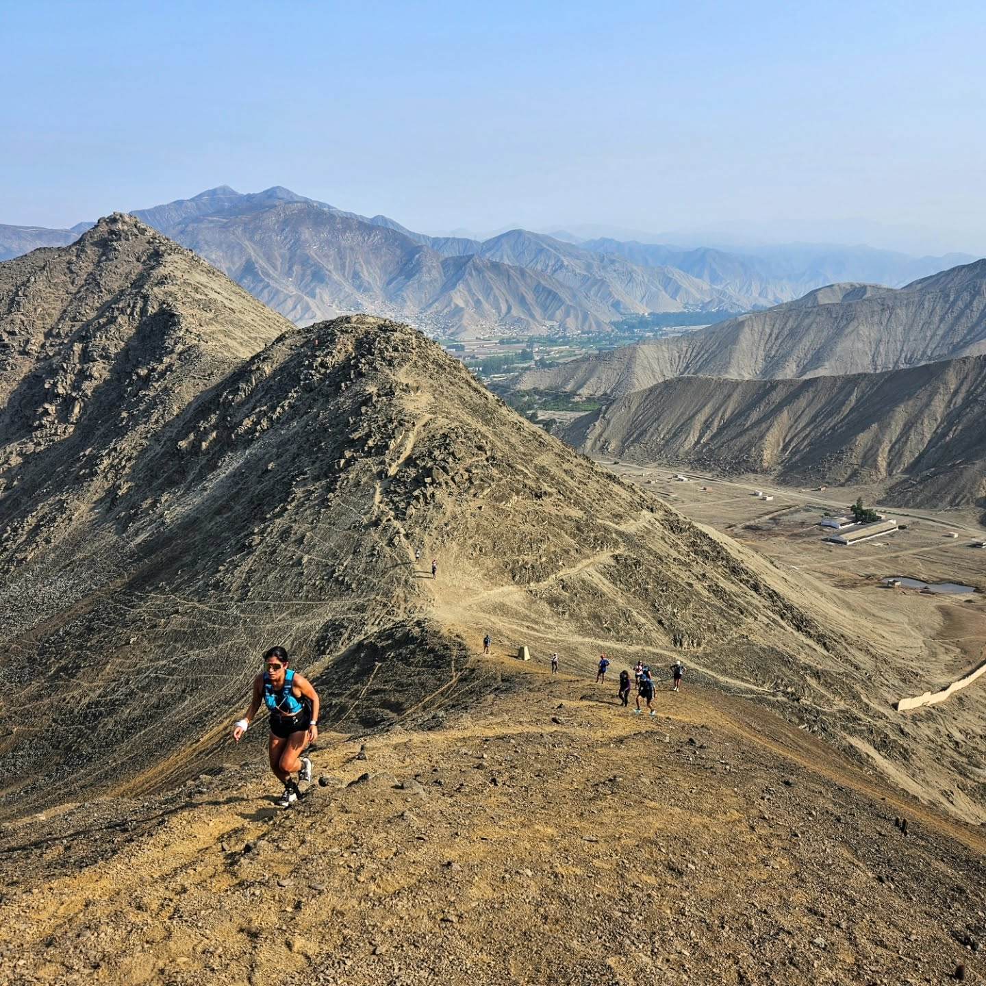 Corredora subiendo en solitario una cresta de cerro seco con el valle y la cordillera al fondo
