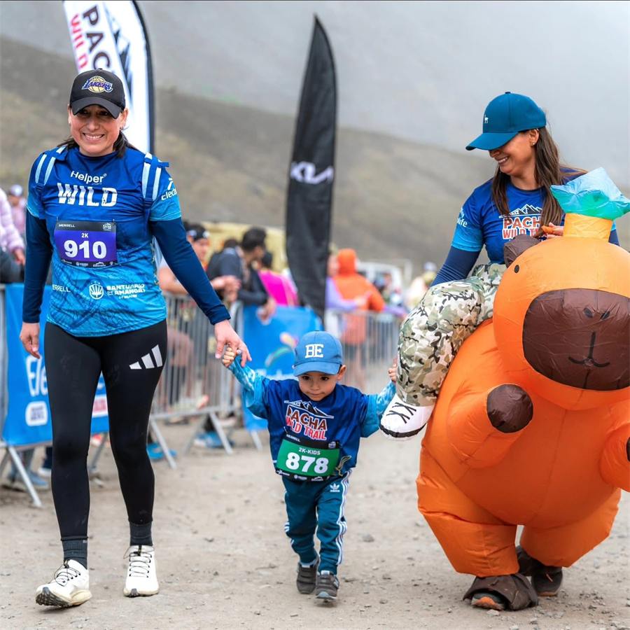 Niño con dorsal caminando hacia la meta acompañado de su familia y la mascota del evento