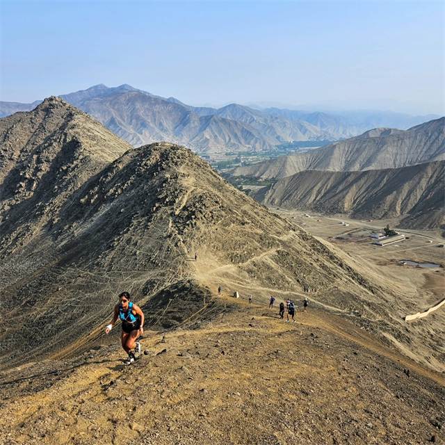 Corredora subiendo una cresta seca con el valle y las montañas al fondo