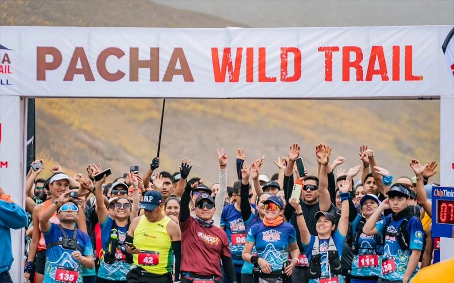 Corredores celebrando bajo el arco de partida de Pacha Wild Trail con el cerro seco de verano al fondo