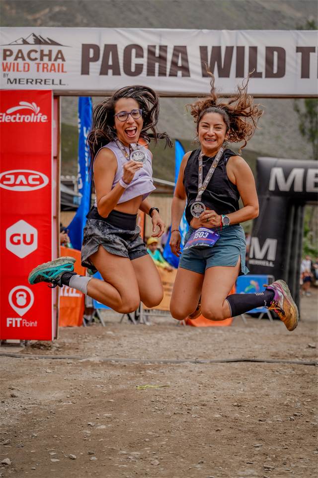 Dos corredoras saltando con sus medallas bajo el arco de meta